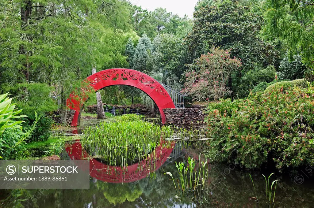 Usa, Alabama, Red Arched Bridge Crossing Tranquil Water In Park; Mobile