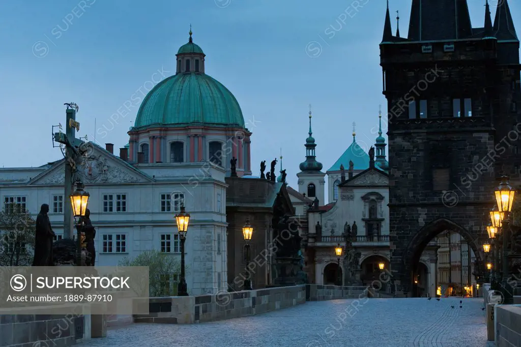 Czech Republic, Cross And Statue Monument With Lamp Posts Along Path Illuminated At Dusk; Prague