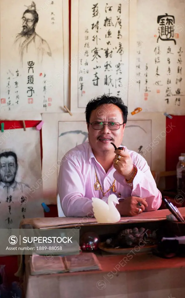 Thailand, Man Smoking Pipe While Sitting At Desk In Chinese Village Near Pai; Shandicun