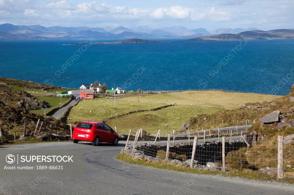 A car travels the road with a view of the ocean between eyeries and allihies;County cork ireland
