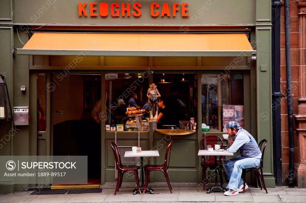 A man sits at an outdoor table of a cafe sipping coffee;Dublin county dublin ireland