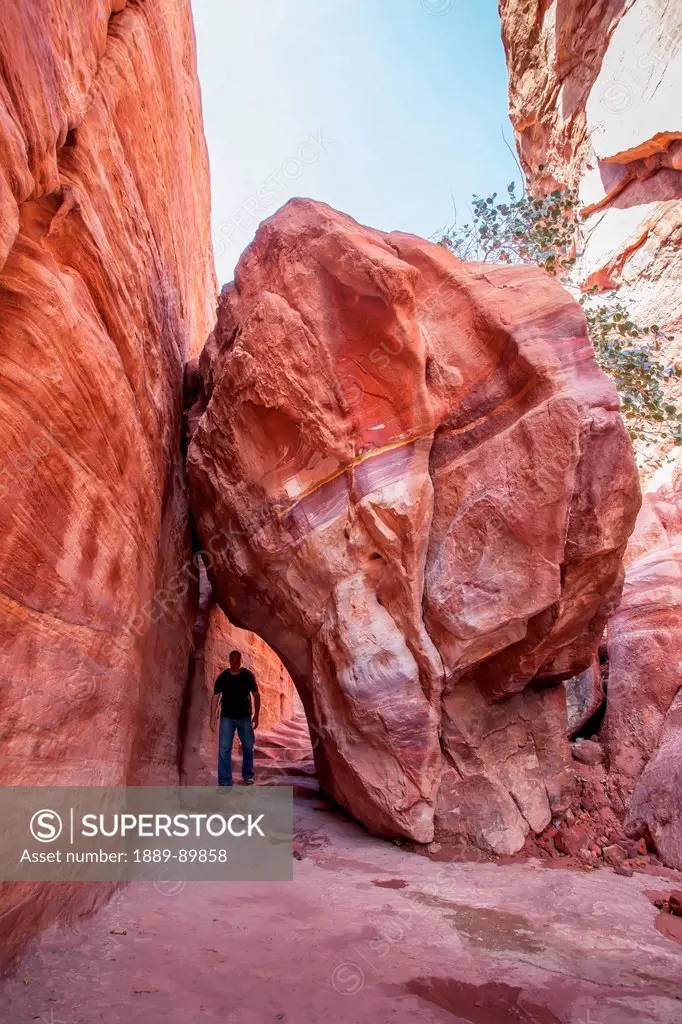 Tourist walking under boulder; Petra, Jordan