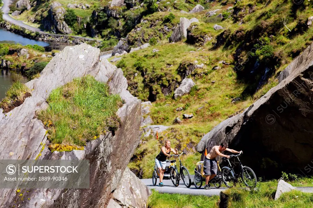 Cyclists ride their way up a winding road in a rocky rugged area at the gap of dunloe;Killarney county kerry ireland
