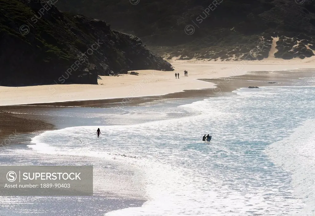 Portugal, Carrapateira, distant view; Playa do Amado, Surfers in water and people walking on beach