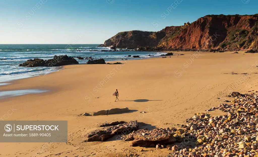 Portugal, Algarve, Distant view of surfer walking on Playa do Amado; Carrapateira