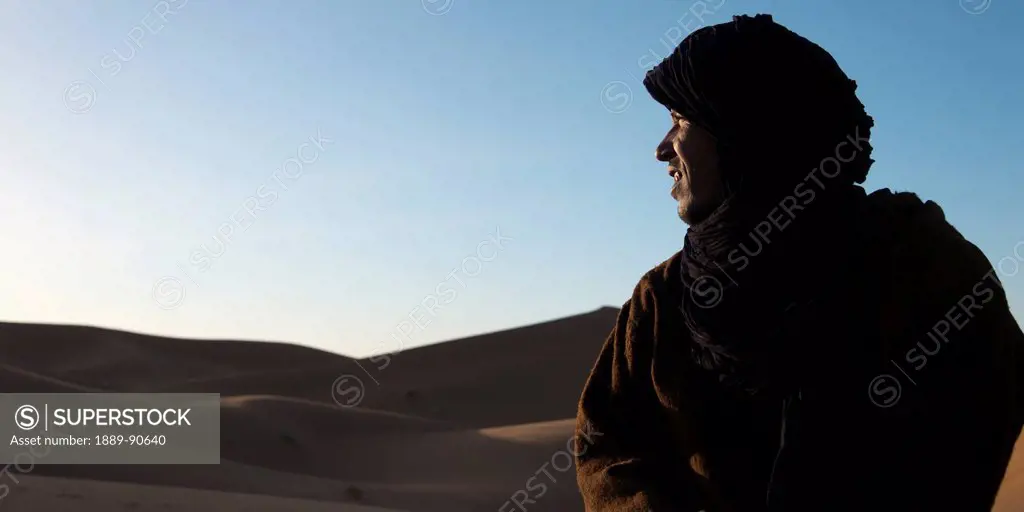 Sunlight shines in the face of a man as he looks over the Erg Chegaga Dunes; Souss-Massa-Draa, Morocco
