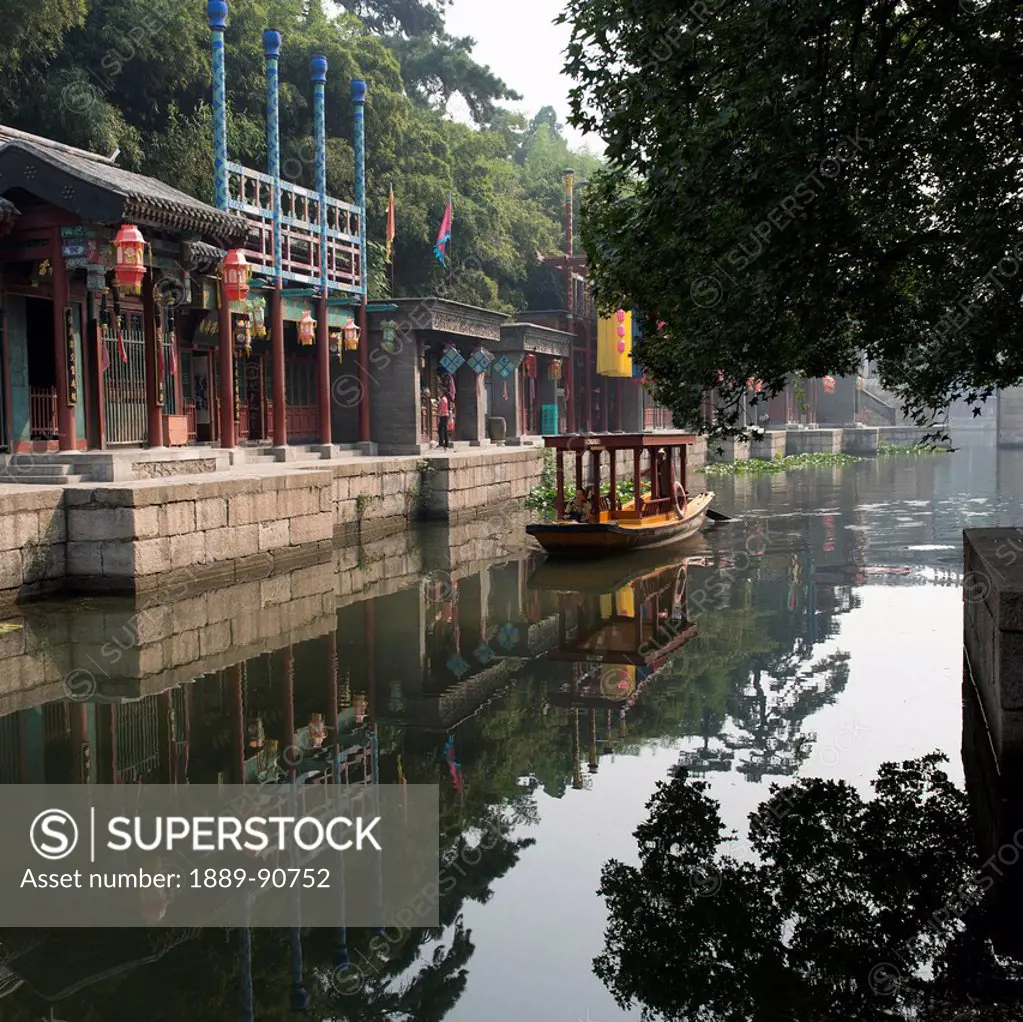 A boat in the tranquil river water and buildings along the water's edge; Beijing, China