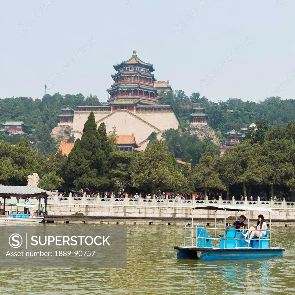 A couple in a boat on Kunming Lake with Tower of Buddhist Incense in the background at Summer Palace; Beijing, China