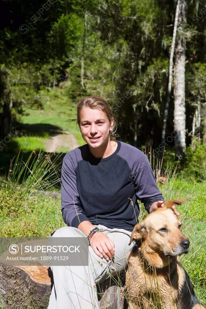 A Girl Sits Relaxing Outside On A Warm Summers Day With Her Dog At Blue Duck Lodge, In Whanganui National Park; Whakahoro, New Zealand