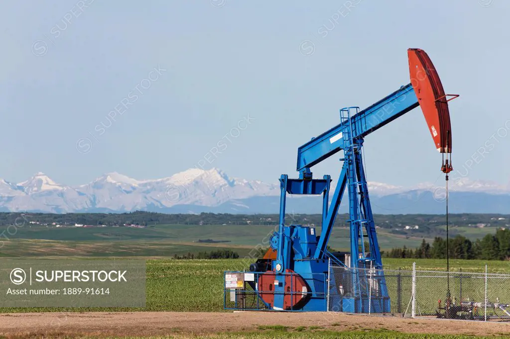 A Pumpjack In A Field With The Rocky Mountains In The Distance; Alberta, Canada