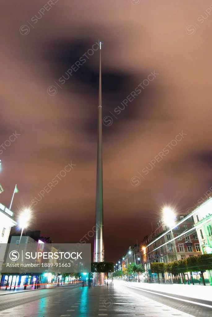 Lights illuminate buildings along a street at nighttime and the Spire of Dublin; Dublin, Ireland