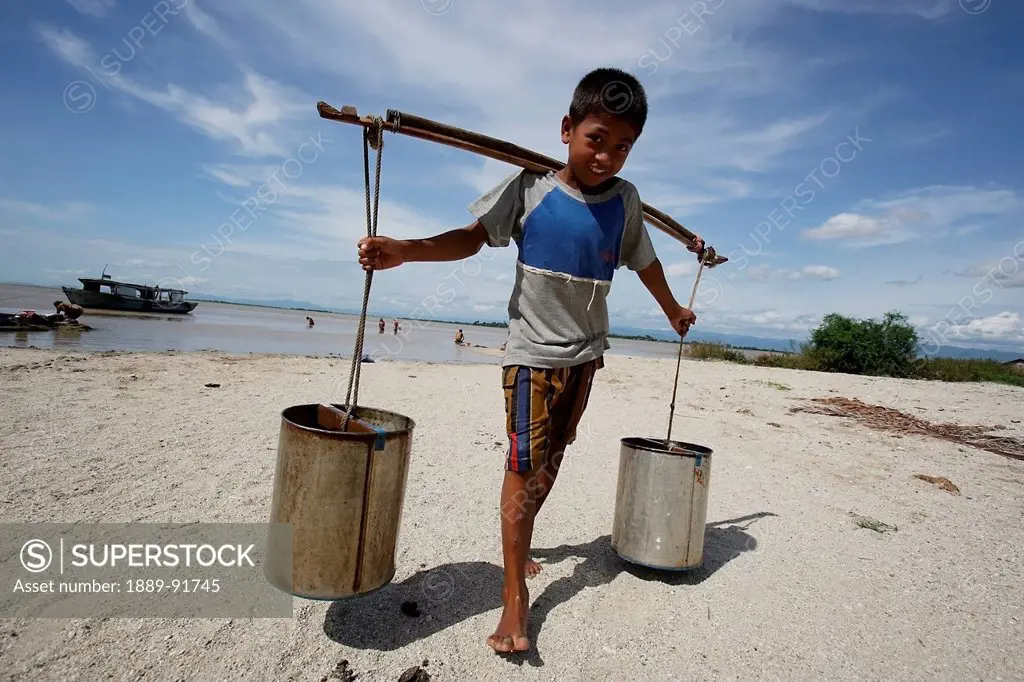 Boy Carries Water In Cans Across His Shoulders From The Ayeyarwady River, Mingun, Myanmar; Ayeyarwady, Burma