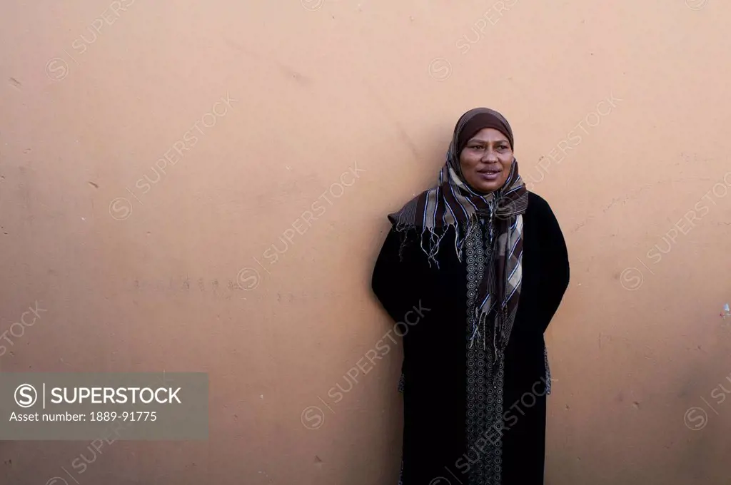 Portrait of a woman wearing a headscarf and standing against the wall; Mfuleni, South Africa