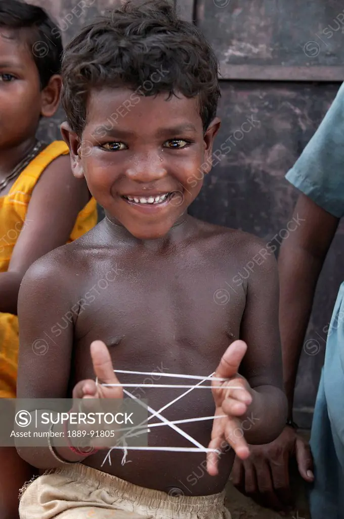A child plays cats cradle with string; India