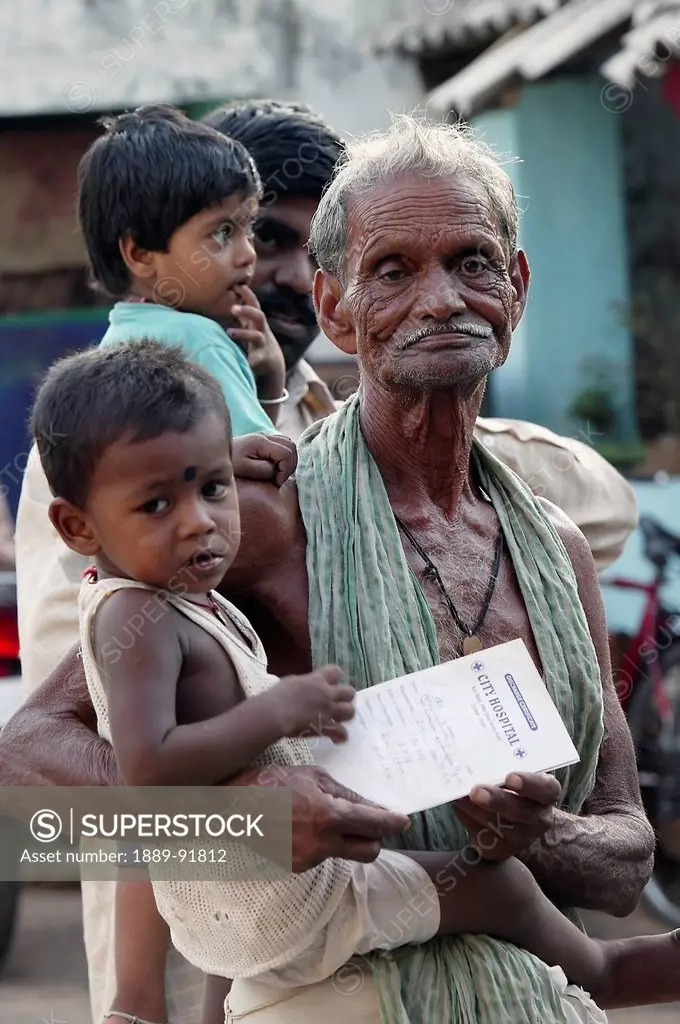 A grandfather holds a grandson with his birth certificate; Cuttack, Odisha, India