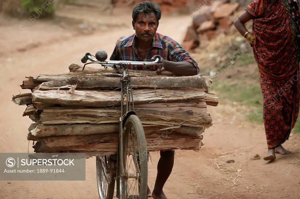 Man pushing heavy load of firewood for sale in the village; Ratapata Village, Badamba, India