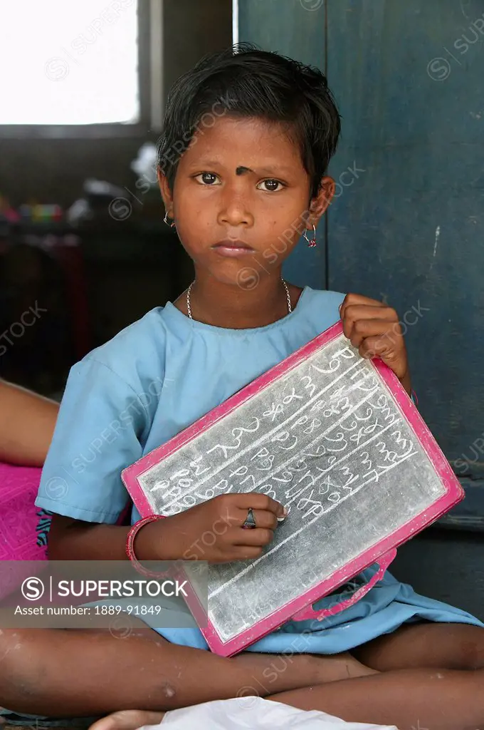 Preschooler practising letters and numbers on a slate board; Ichhapur village, India