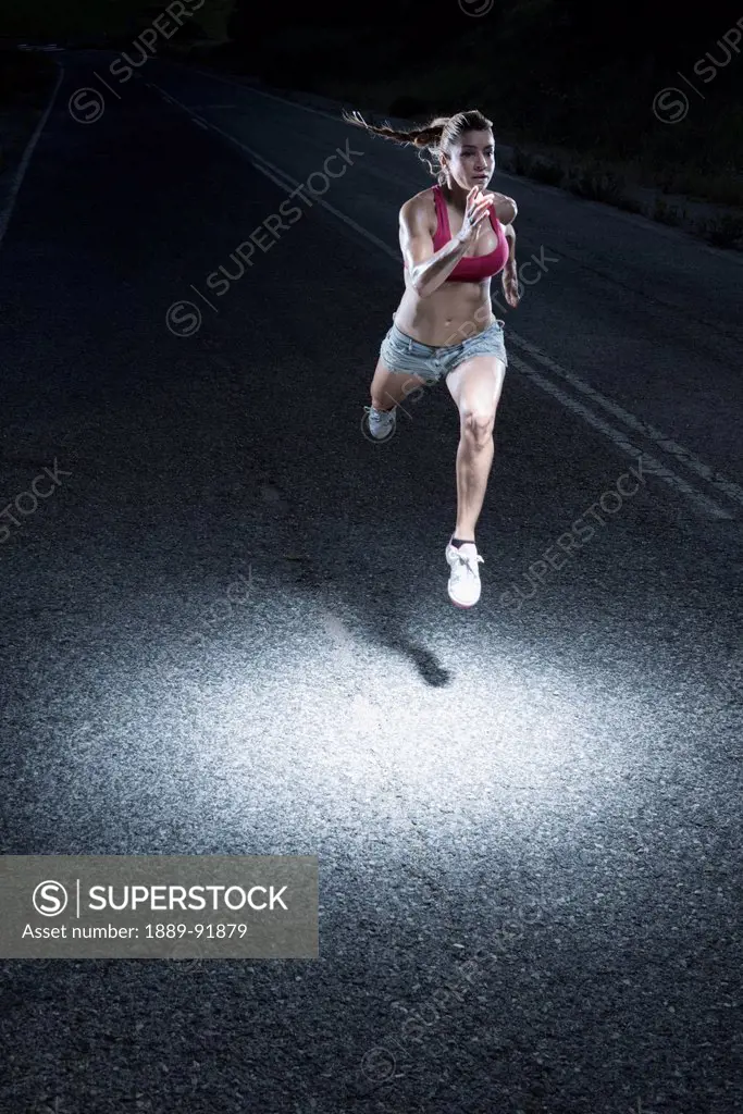A Woman Running Down A Paved Road At Night With A Spotlight Illuminating Her; Tarifa, Cadiz, Andalusia, Spain