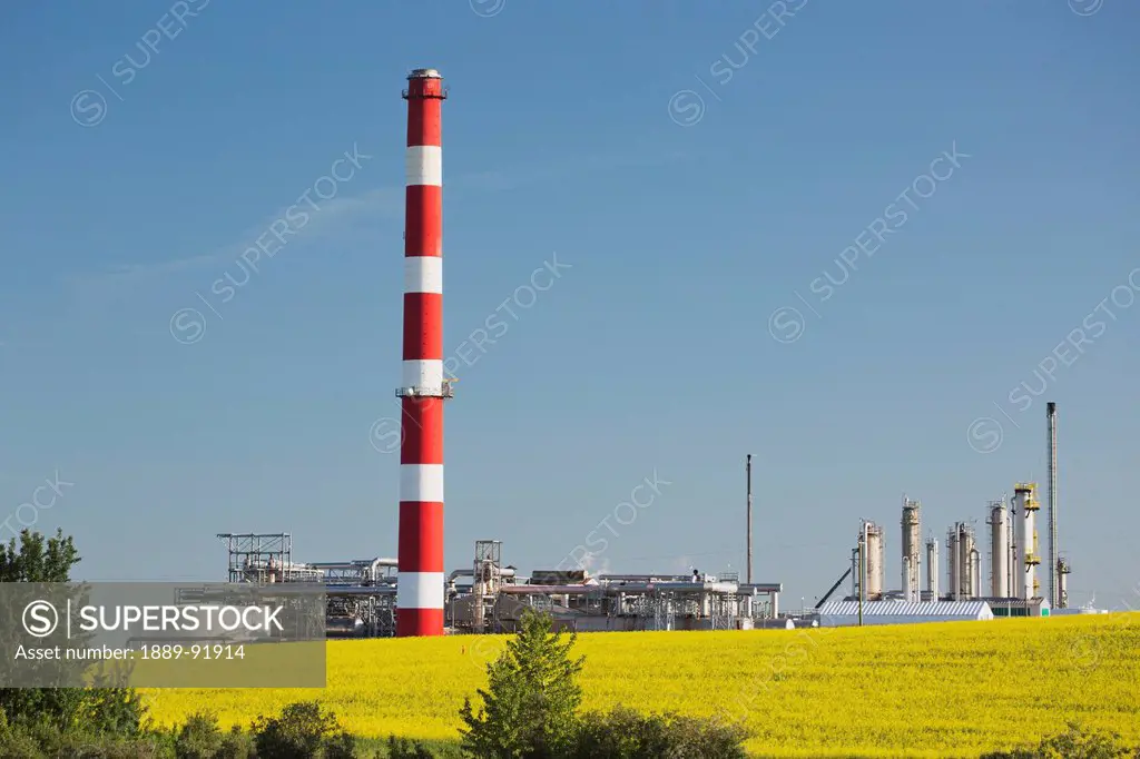 A Tall Tower At A Refinery Next To Farmland; Alberta, Canada