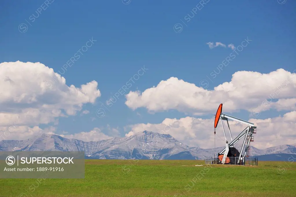 A Pumpjack In A Field With The Rocky Mountains In The Background; Alberta, Canada