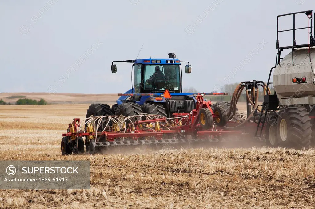 Close Up Of An Air Seeder In A Field With A Tractor And Blue Sky In The Background; Acme, Alberta, Canada