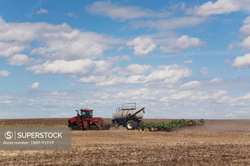 An Air Seeder In A Field With A Tractor And Blue Sky With Cloud; Acme, Alberta, Canada
