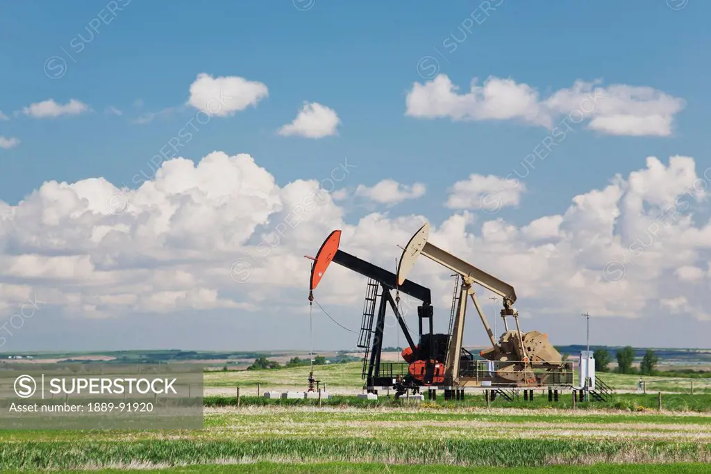 Two Pump Jacks In A Field With Clouds And Blue Sky; Acme, Alberta, Canada