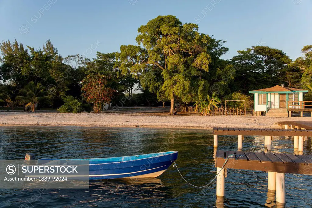 A Motorboat Tied To A Wooden Dock Off The Shore Of An Island; Bay Islands, Honduras