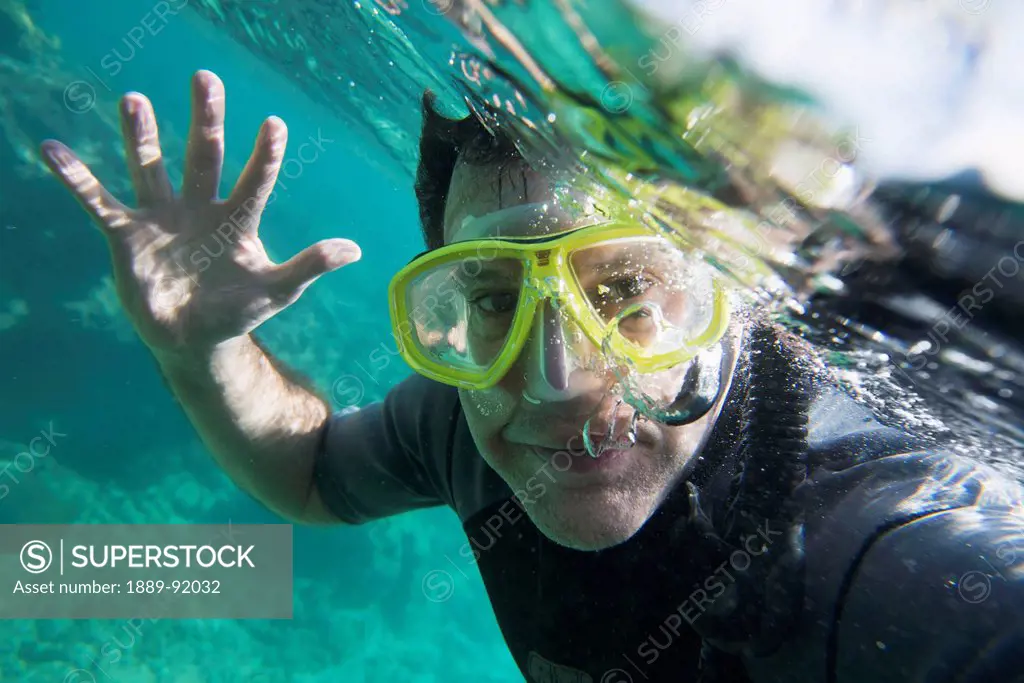 A Male Scuba Diver Waves Hello Underwater; Utila Island, Honduras