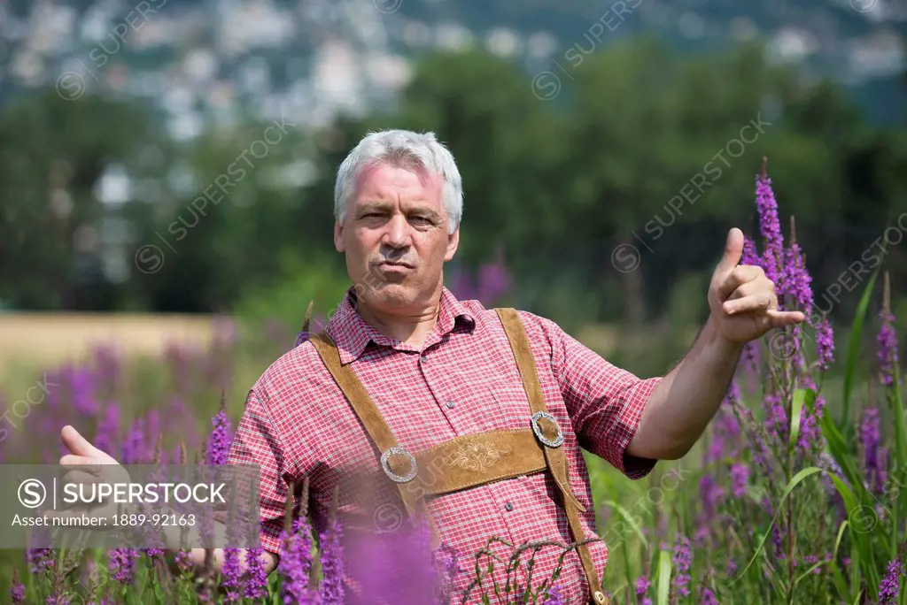 A Man Standing In A Field With Purple Blossoms Giving The Shaka Sign With His Hands; Locarno, Ticino, Switzerland