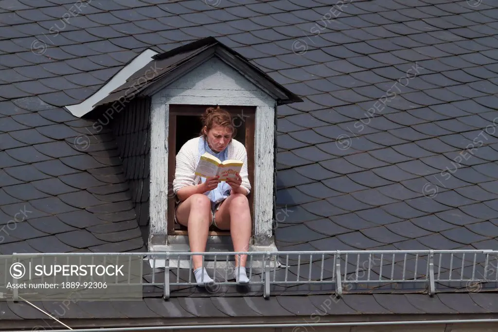 Woman reading in a window of a mansard roof, Mainz, Germany