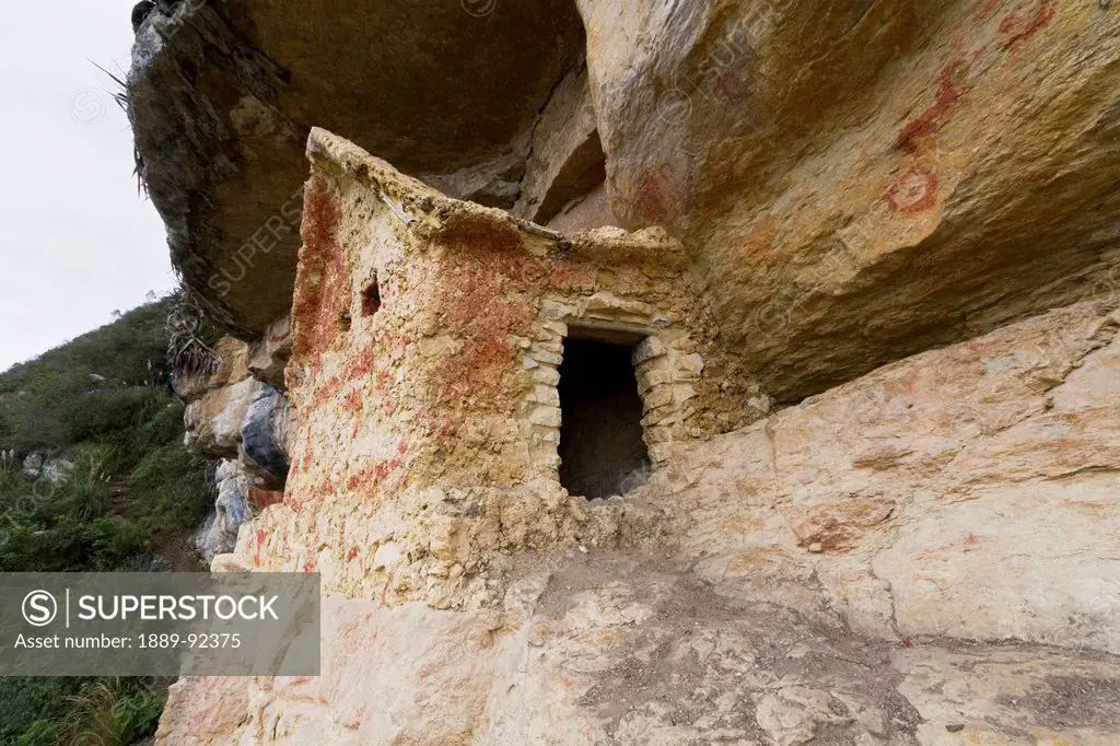 Chullpa (stone tomb chamber) of the Chachapoya culture with walls colored with red figures, nestled in the limestone cliffs of Cerro Carbón overlookin...