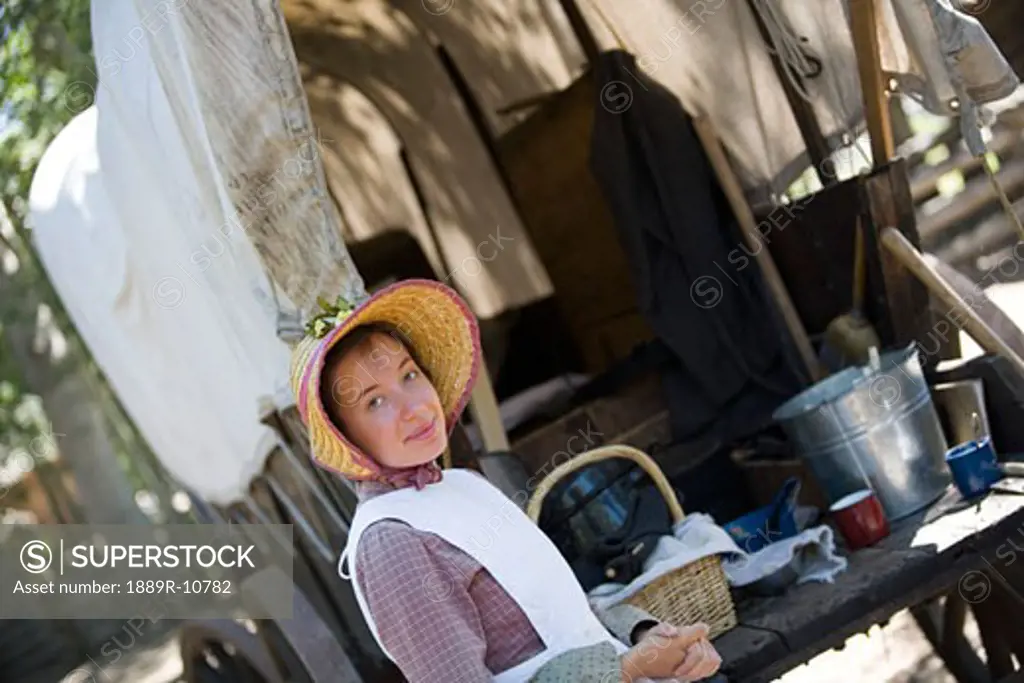 Woman in old-fashioned clothing beside covered wagon