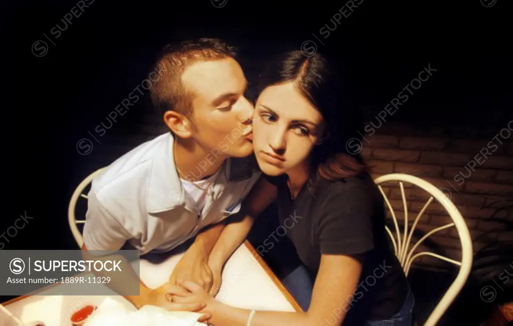 Man kissing an unhappy woman on the cheek