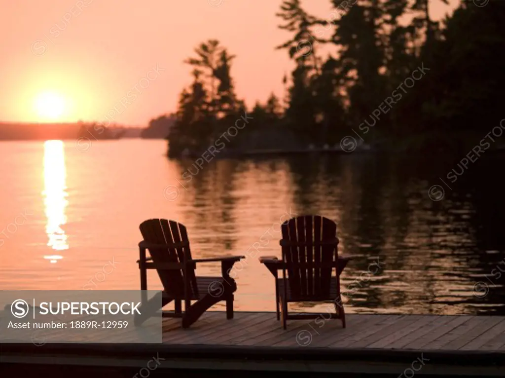 Lake of the Woods, Ontario, Canada, Adirondack chairs on a dock facing the sunset