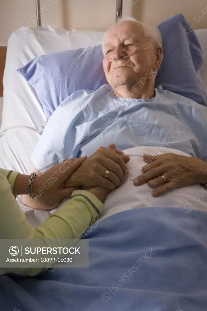 Man in a hospital bed; Man's hand being held by a woman