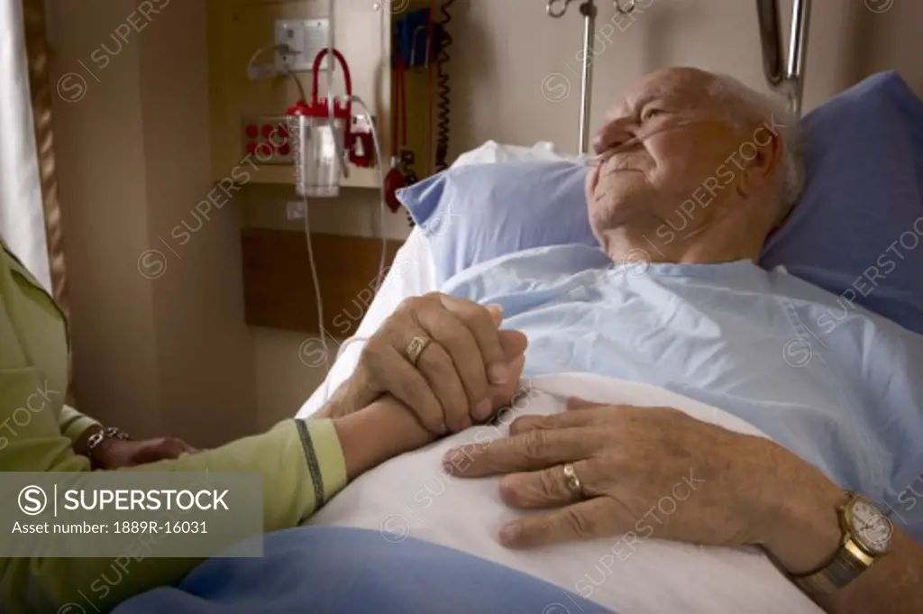 Man in a hospital bed; Man's hand being held by a woman