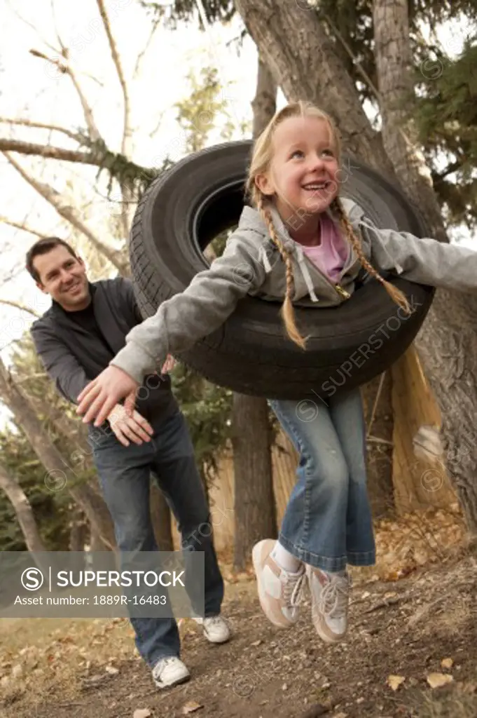 Father pushing daughter on tire swing