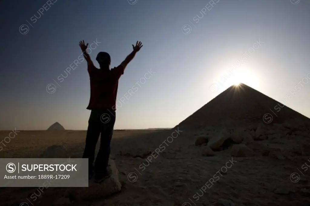 Dahshur, Egypt; Man with arms raised in front of the Red Pyramid