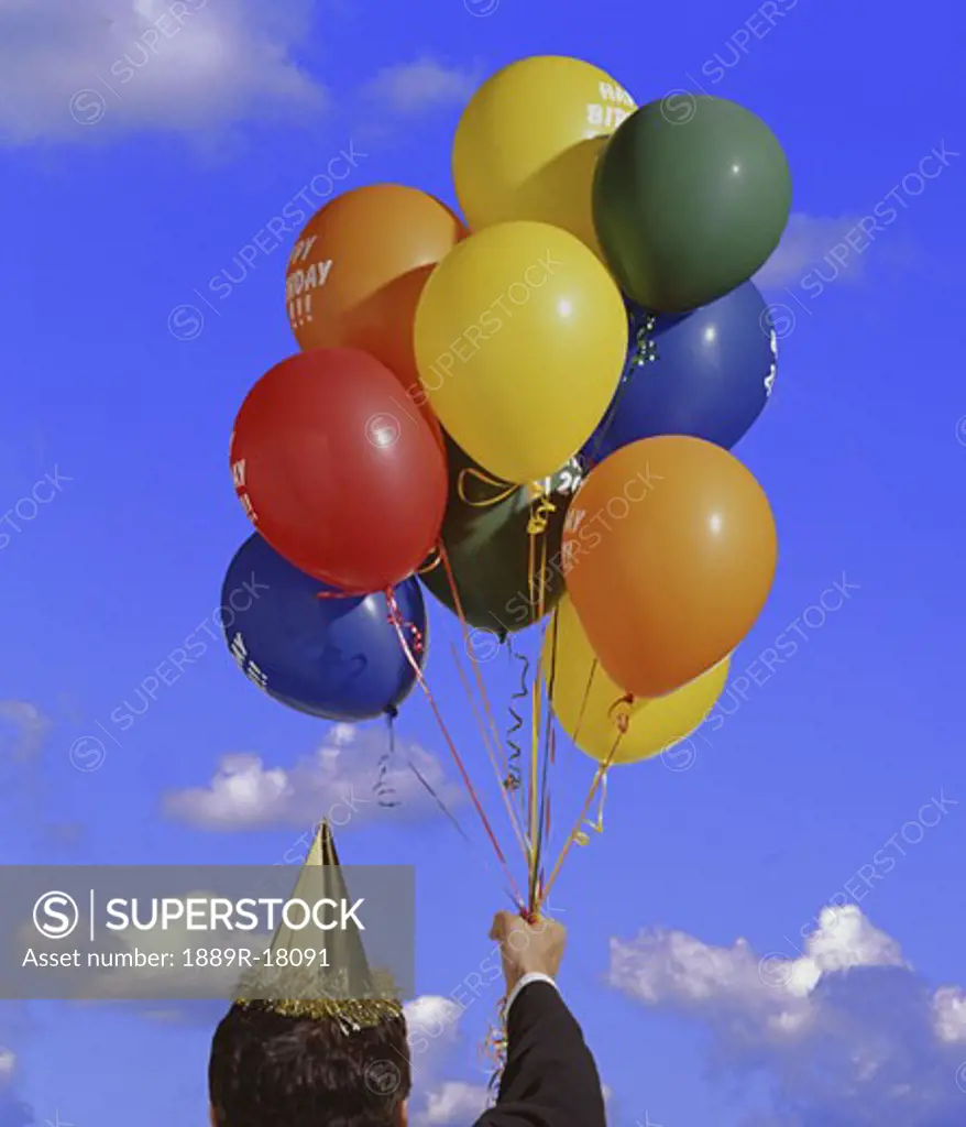 Man holding balloons and party hat
