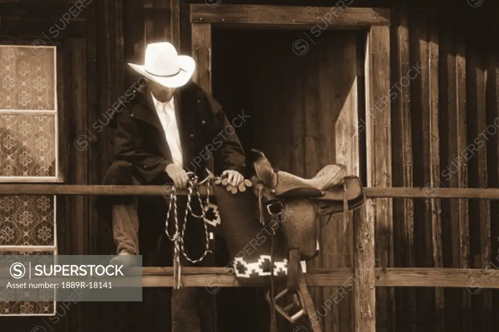 Cowboy with saddle and lariat over handrail in front of building