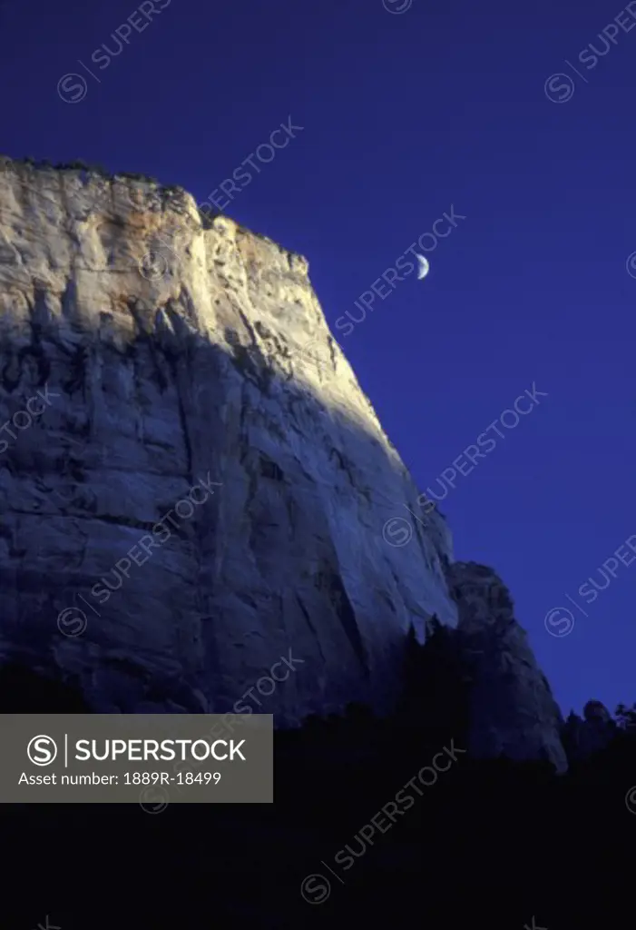 Mountain cliff with deep blue sky and quarter moon