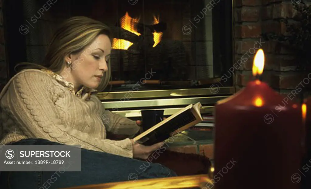 Young woman reading book in front of fireplace