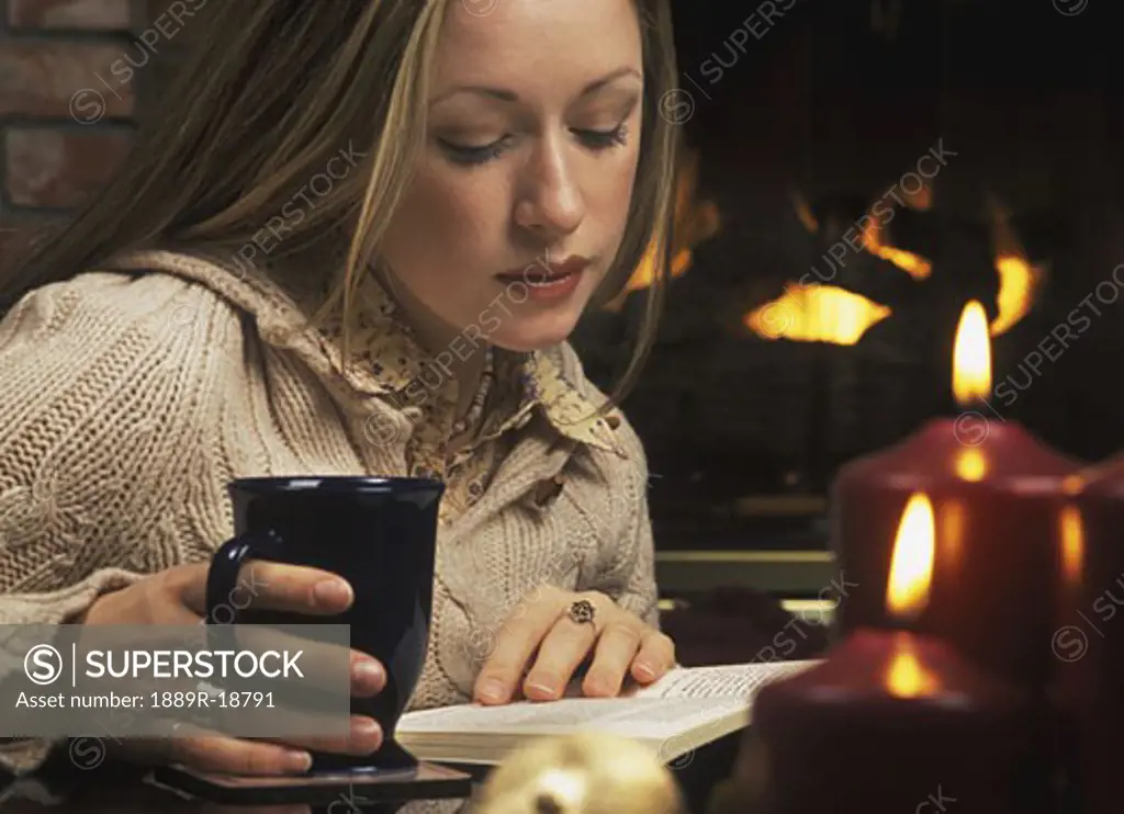 Young woman reading book in front of fireplace