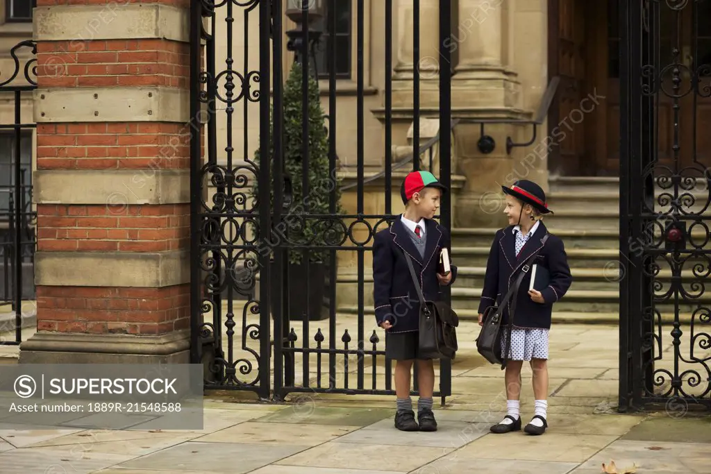 Young boy and girl students in uniform talking outside the school; London, England