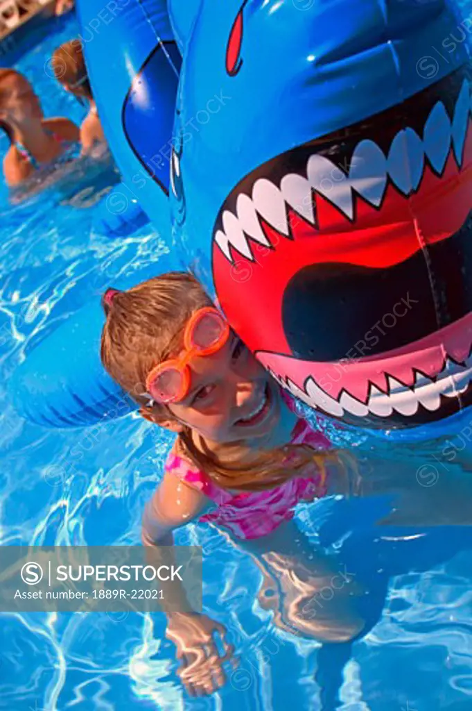 Girl playing in swimming pool with inflatable shark