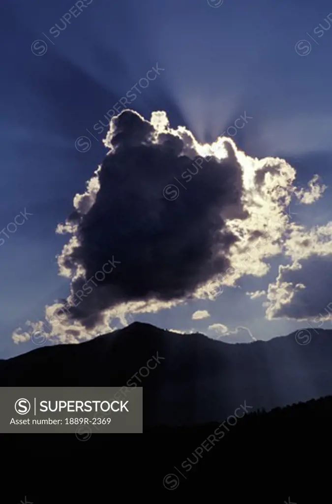 Sun behind a cloud above mountain range