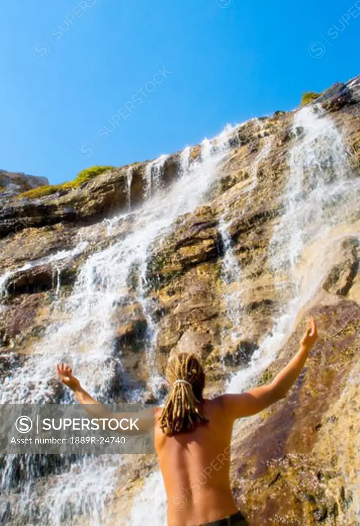 Man standing under waterfall with outstretched arms
