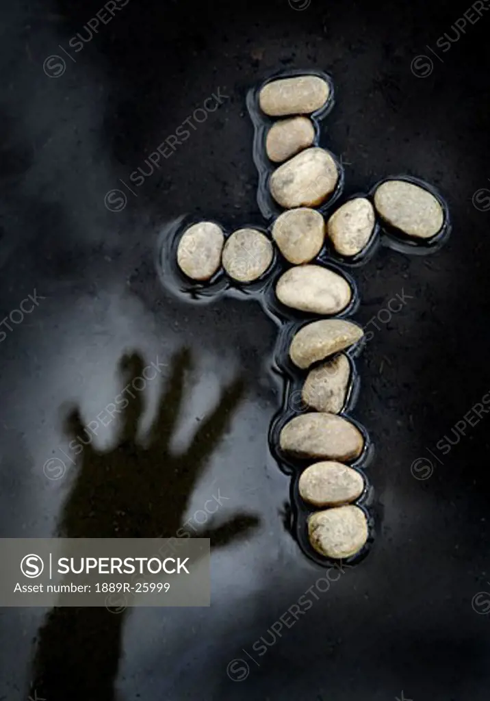 Hand reaching over water for cross made of rocks