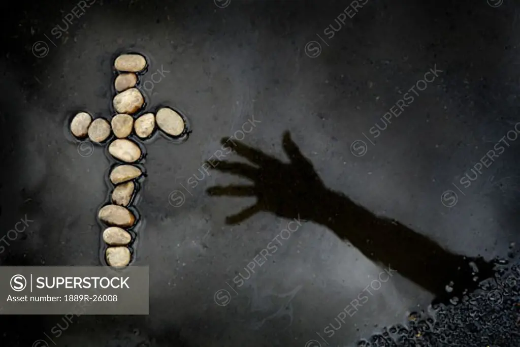 Hand reaching into water for cross made of rocks